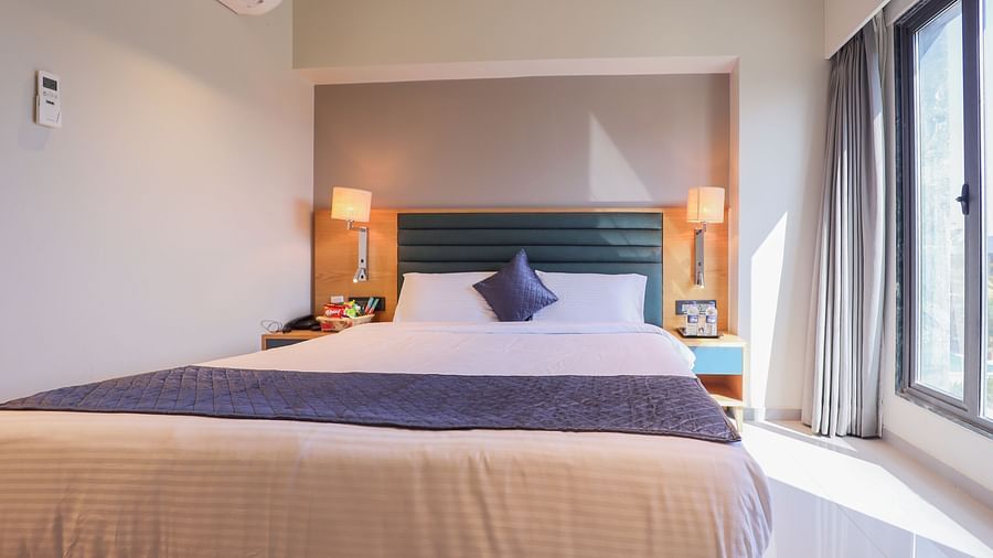 An image of a bedroom with double size bed, bedside lamp on either side, and an window - Pride Resort Ambaji